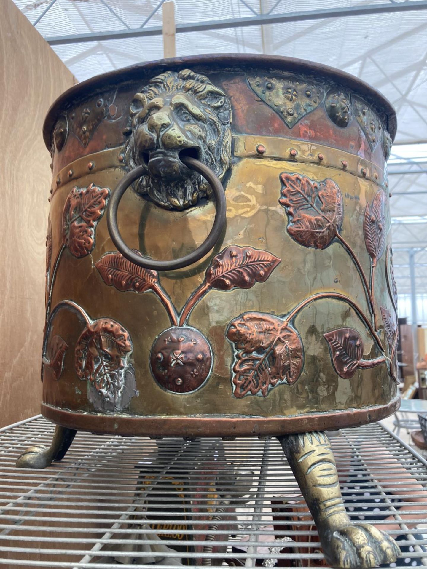 A VERY LARGE DECORATIVE BRASS AND COPPER BUCKET ON THREE CLAW FEET AND LION DESIGN HANDLES WITH