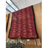 A SMALL RED PATTERNED FRINGED RUG