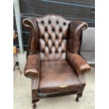 A BROWN BUTTON AND WINGED BACK FIRESIDE CHAIR