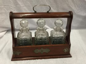 A MAHOGANY TANTALUS WITH BRASS DETAILING AND THREE CUT GLASS DECANTERS. COMES WITH KEY BUT WILL