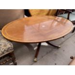 AN OVAL MAHOGANY AND CROSSBANDED COFFEE TABLE ON PEDESTAL BASE WITH BRASS CASTERS, 48X28"