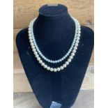 TWO STRINGS OF PEARLS WITH SILVER CLASPS ON A PRESENTATION STAND