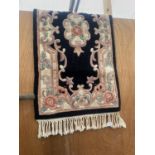 A SMALL BLACK PATTERNED FRINGED RUG