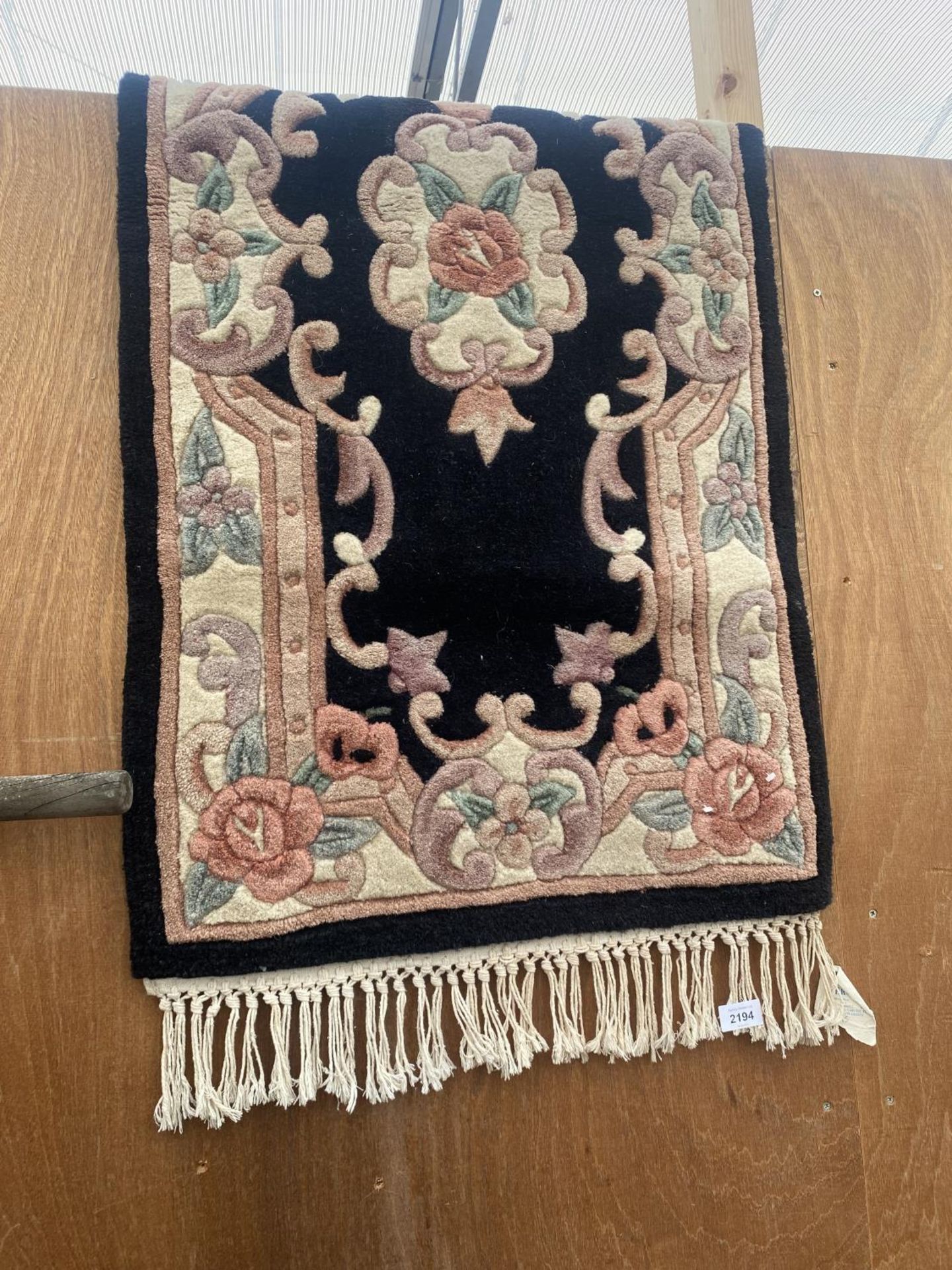 A SMALL BLACK PATTERNED FRINGED RUG