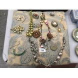 A QUANTITY OF COSTUME JEWELLERY ON A CUSHION TO INCLUDE NECKLACES AND VINTAGE BROOCHES SET WITH