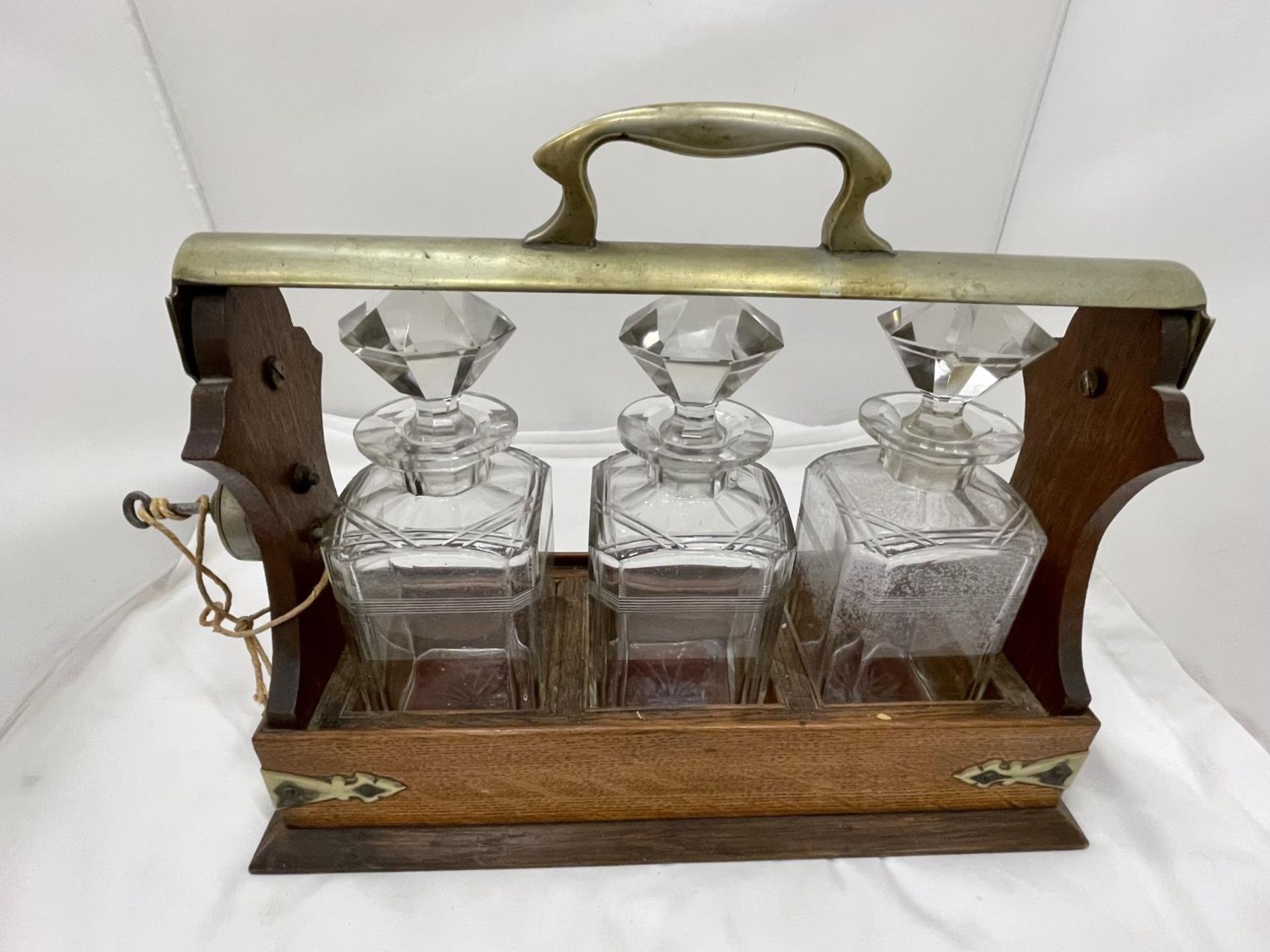 A VINTAGE MAHOGANY AND BRASS TANTALUS WITH THREE MATCHING DECANTERS AND KEY