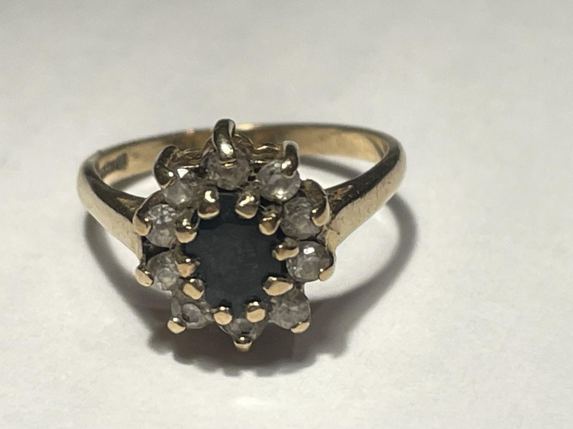 A 9 CARAT GOLD RING WITH A CENTRE SAPPHIRE SURROUNDED BY CLEAR STONES SIZE I