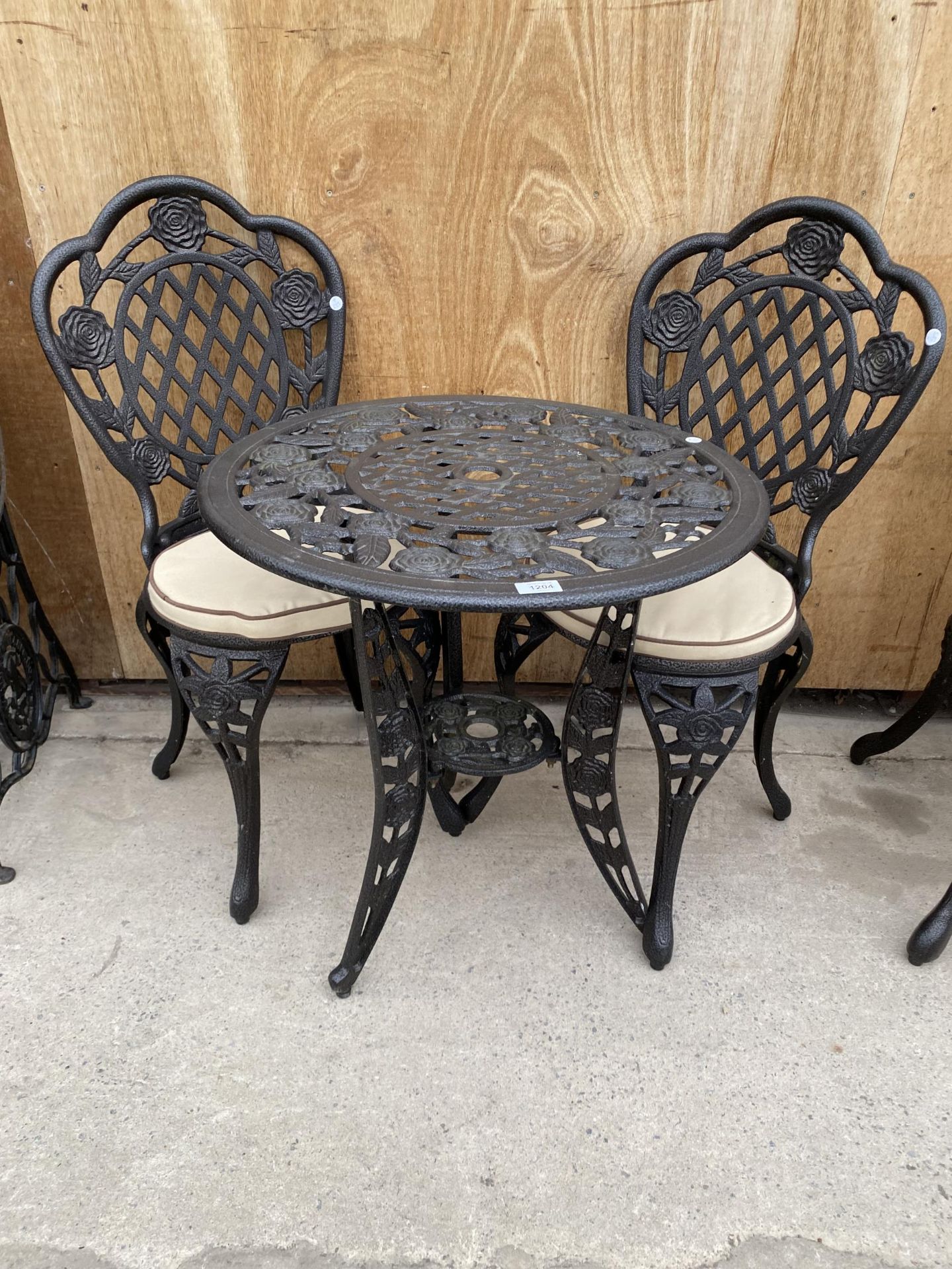 A CAST ALLOY BISTRO SET COMPRISING OF A ROUND FLORAL TABLE AND TWO CHAIRS WITH CUSHIONS