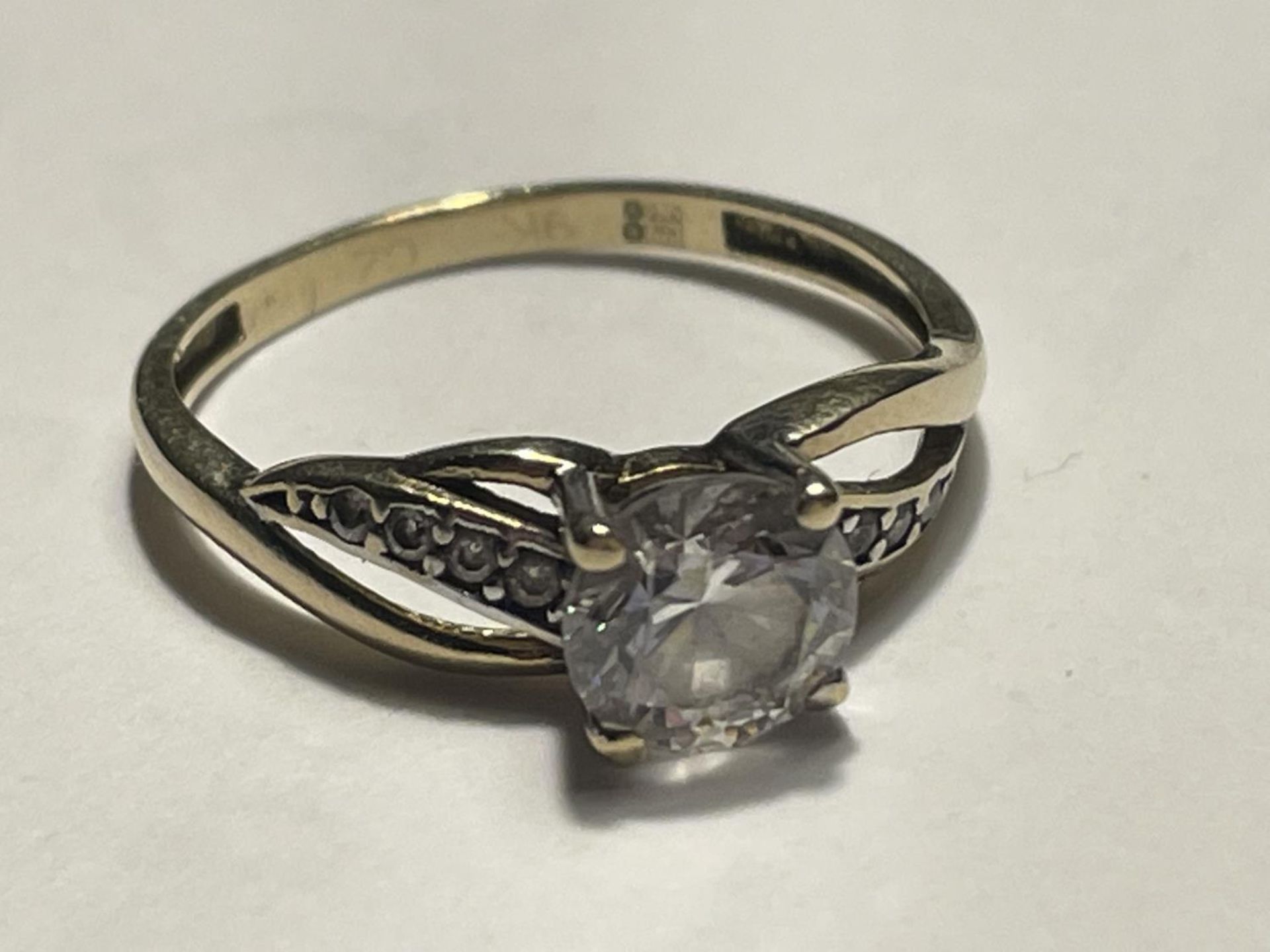 A 9 CARAT GOLD RING WITH A LARGE CENTRE CLEAR STONE AND SMALLER TO THE SHOULDERS