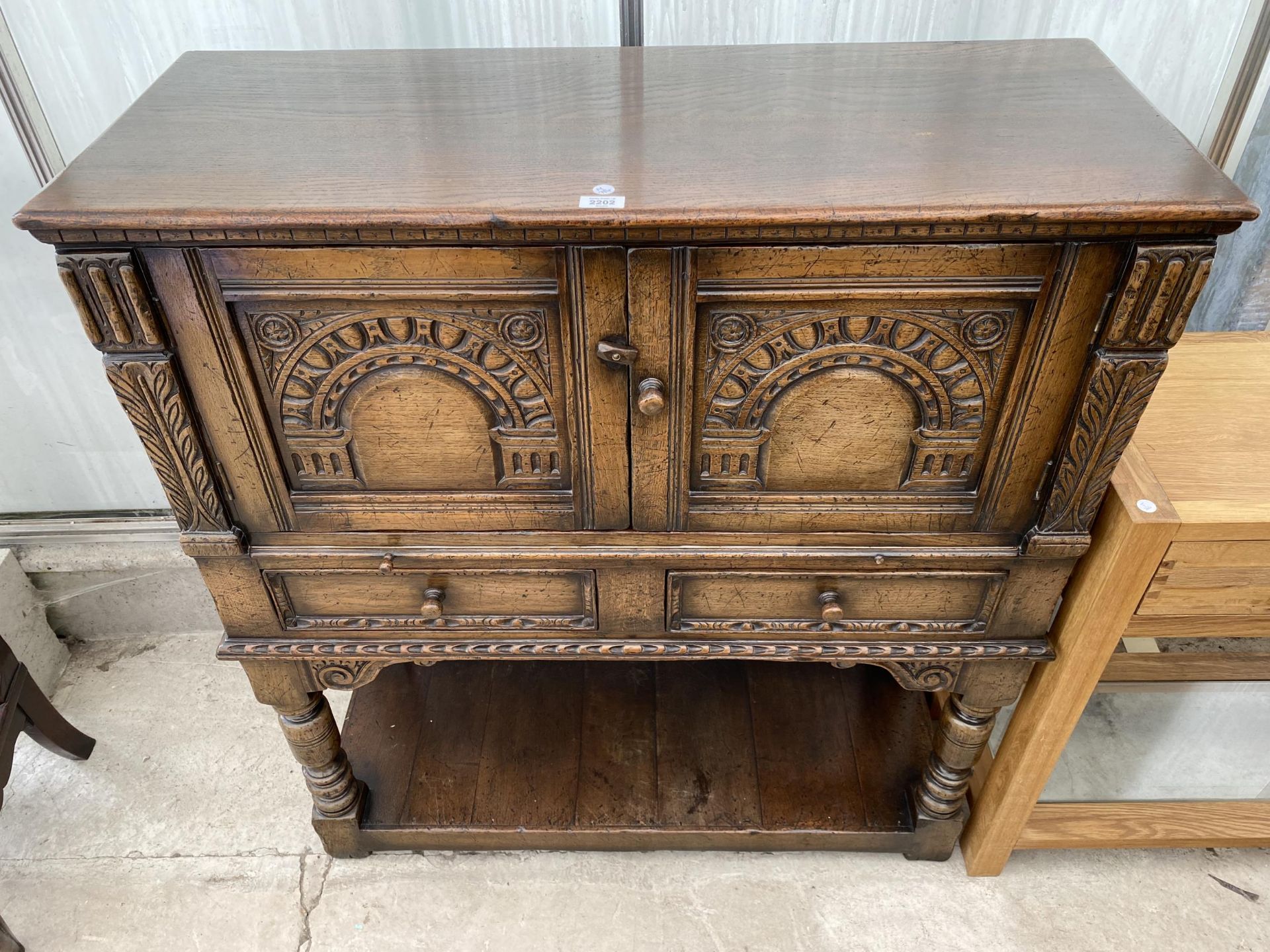 AN OAK JACOBEAN STYLE COCKTAIL CABINET WITH PANELLED DOOR, PULL OUT SLIDE, TWO DRAWERS AND A POT