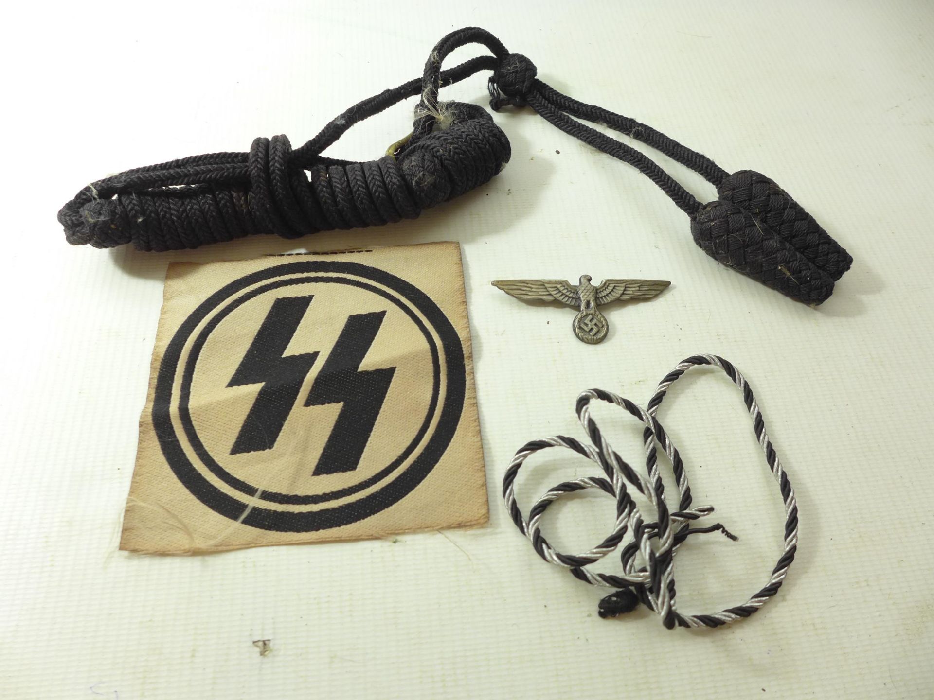 A NAZI GERMANY SS CLOTH BADGE, TWO LOTS OF BRAID AND AN EAGLE & SWASTIKA BADGE