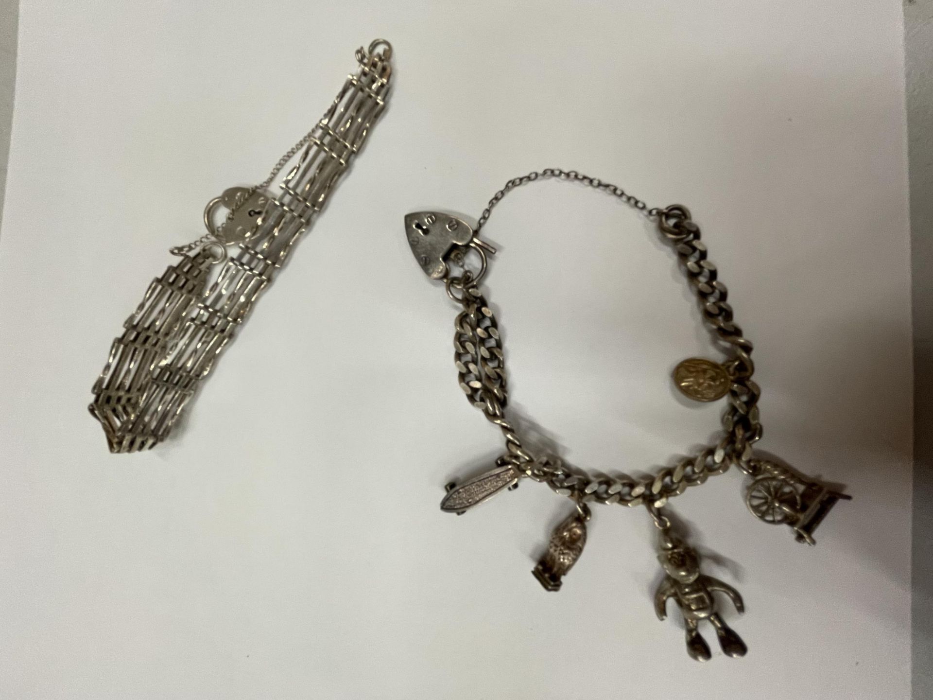 TWO SILVER BRACELETS TO INCLUDE A CHARM BRACELET WITH FIVE CHARMS AND A FIVE BAR GATE BRACELET