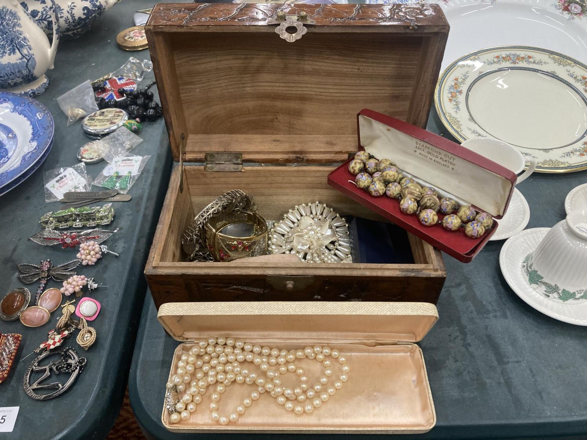 A WOODEN CARVED BOX CONTAINING A QUANTITY OF COSTUME JEWELLERY TO INCLUDE BOXED PEARL NECKLACE,