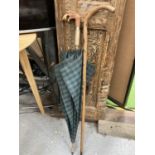 A VINTAGE GREEN TARTAN UMBRELLA WITH A FIGURE HEAD HANDLE PLUS A WALKING STICK WITH ATTACHED