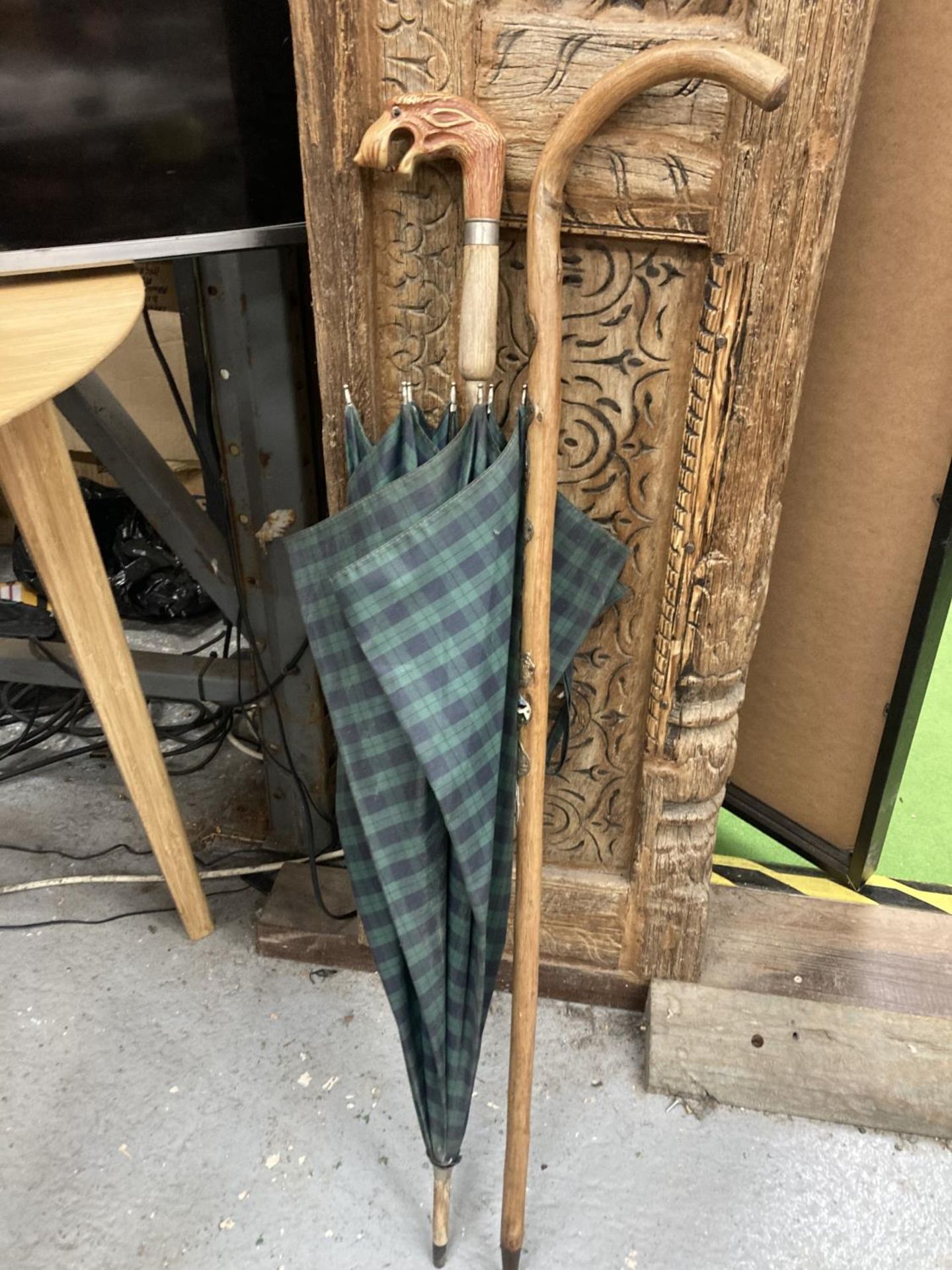 A VINTAGE GREEN TARTAN UMBRELLA WITH A FIGURE HEAD HANDLE PLUS A WALKING STICK WITH ATTACHED