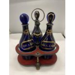 A SET OF THREE GEORGE III GILDED BRISTOL BLUE GLASS DECANTERS IN BRASS AND LAQUERED FRAME