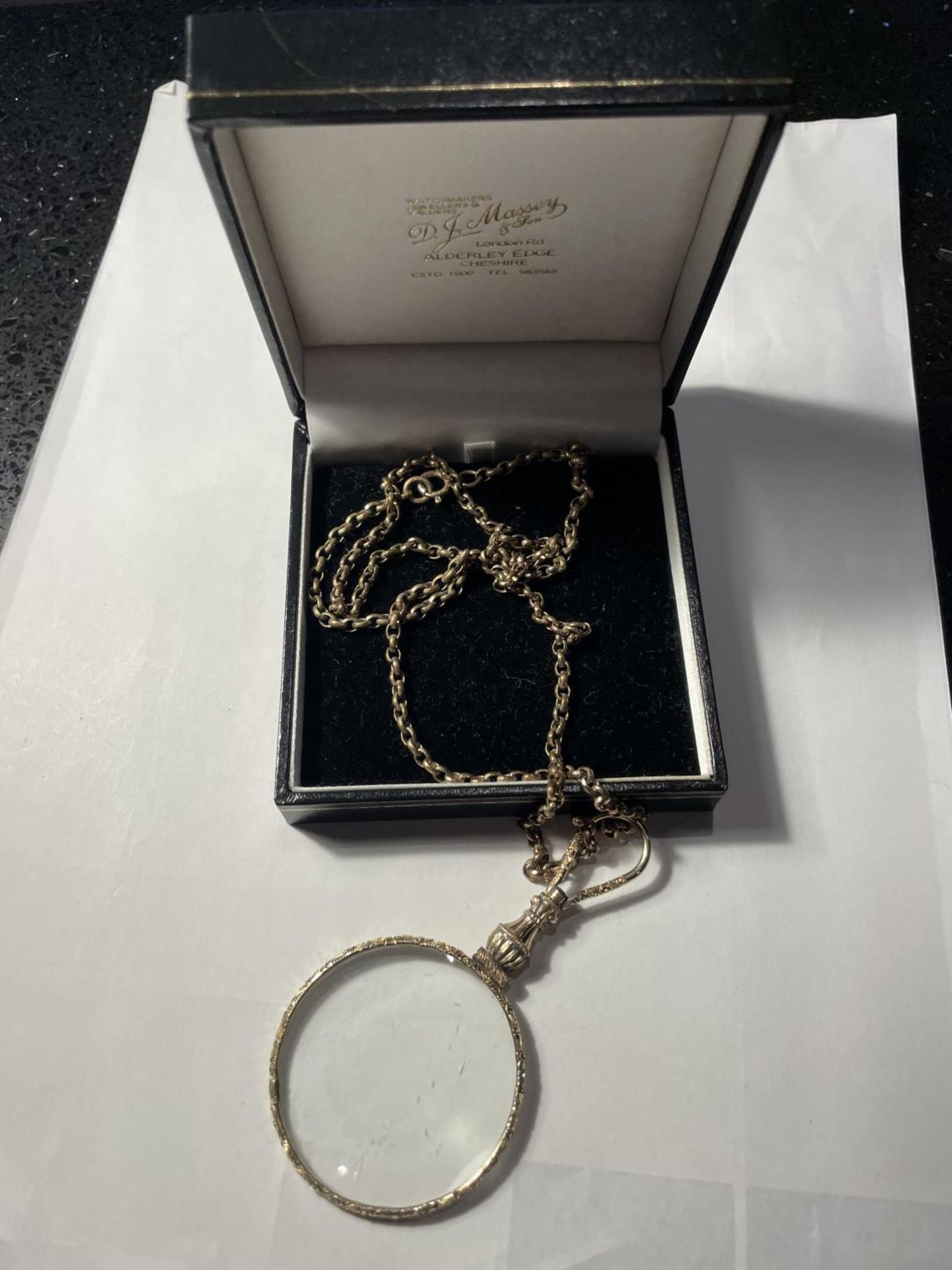 A YELLOW METAL CHAIN WITH A DECORATIVE MAGNIFYING GLASS PENDANT IN A PRESENTATION BOX