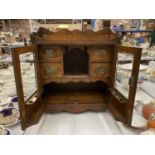 A VINTAGE OAK SMOKERS CABINET WITH BEVELLED GLASS DOORS, BRASS HANDLED DRAWERS, GALLERIED TOP, ETC
