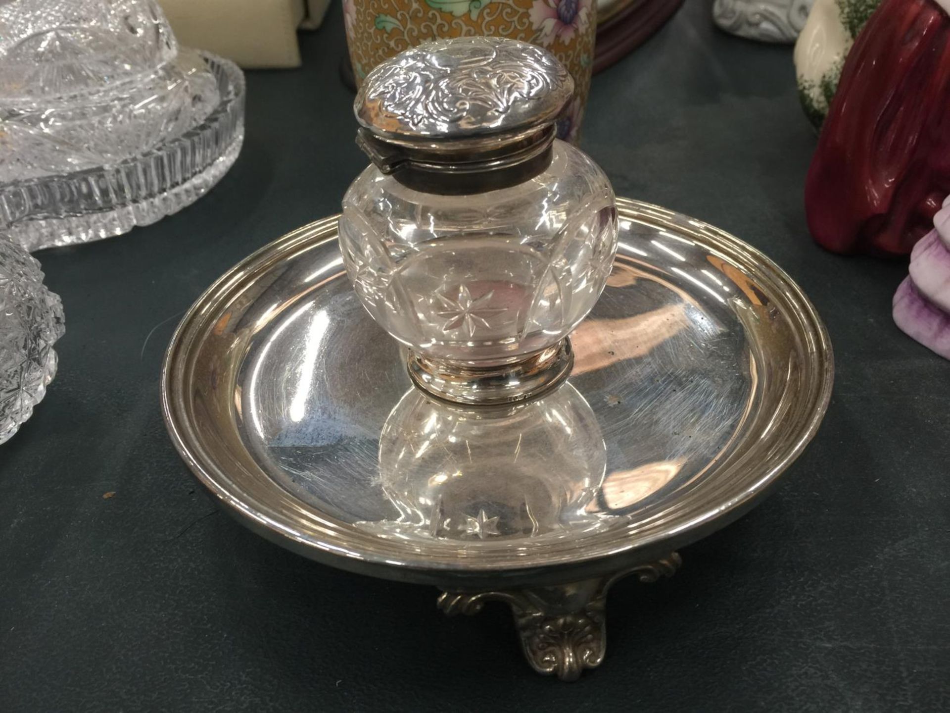 A CUT GLASS AND SILVER PLATED INKWELL FIXED TO A TRAY ON THREE DECOTTIVE FEET