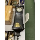 A LARGE WALL CLOCK IN EBONISED CASE WITH CARVED TOP WITH PENDULUM AND WEIGHT