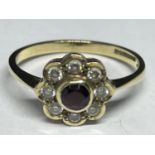 A 9 CARAT GOLD RING WITH A CENTRE RED STONE SURROUNDED BY EIGHT CUBIC ZIRCONIAS IN A FLOWER DESIGN