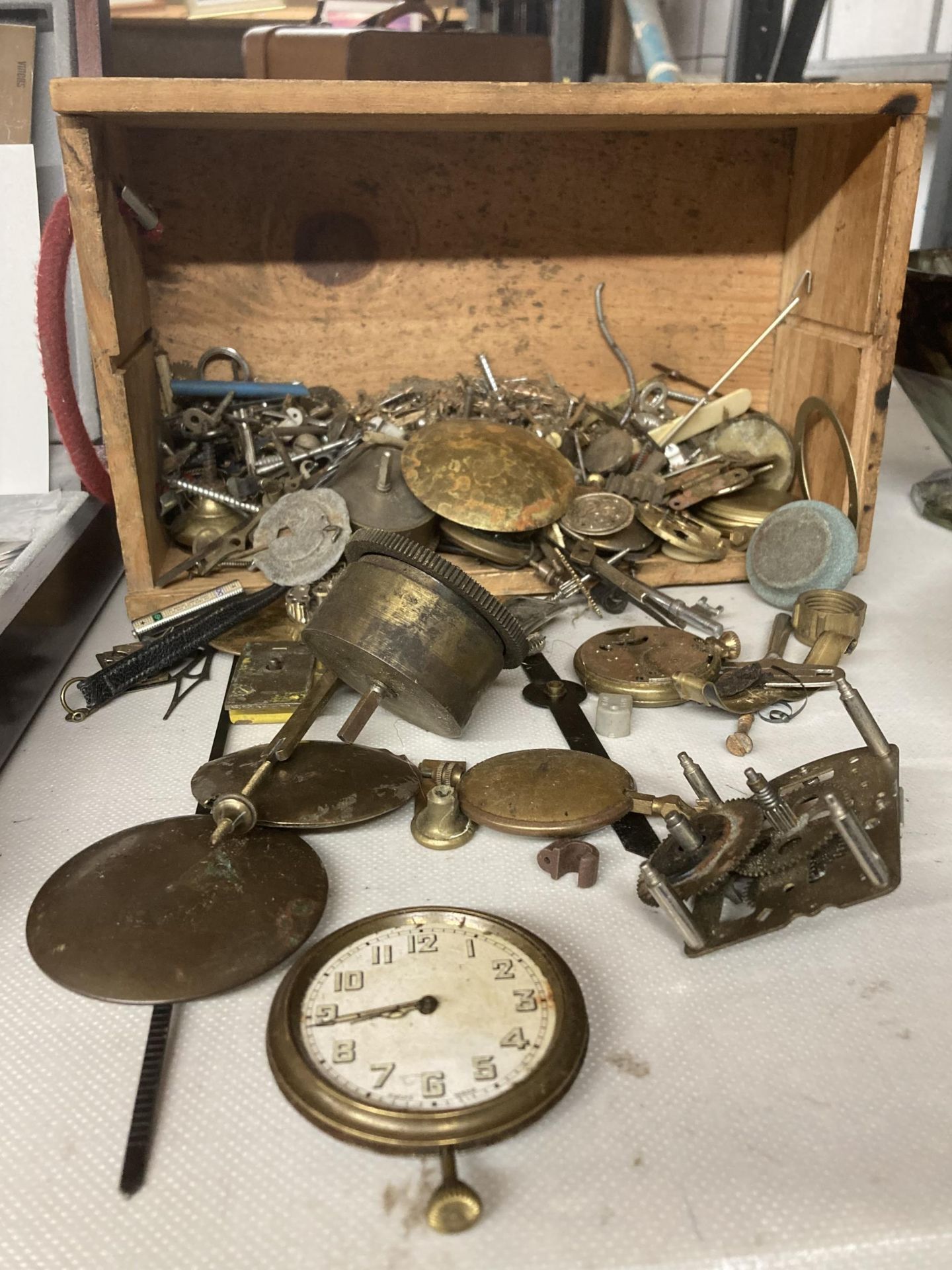 A QUANTITY OF CLOCK AND WATCH SPARE PARTS TO INCLUDE PENDULUMS, KEYS, WATCH FACES, ETC