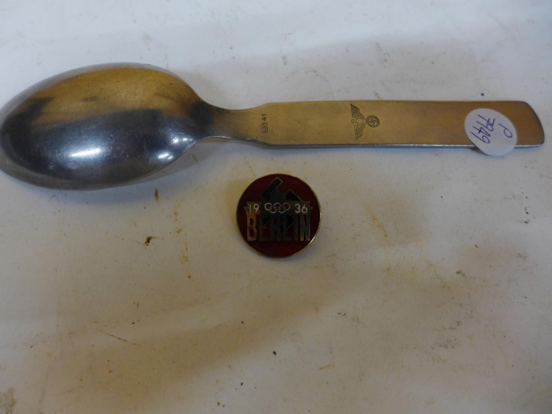A NAZI GERMANY SPOON WITH EAGLE AND SWASTIKA DECORATION AND A NAZE 1936 BERLIN OLYMPICS ENAMEL BADGE