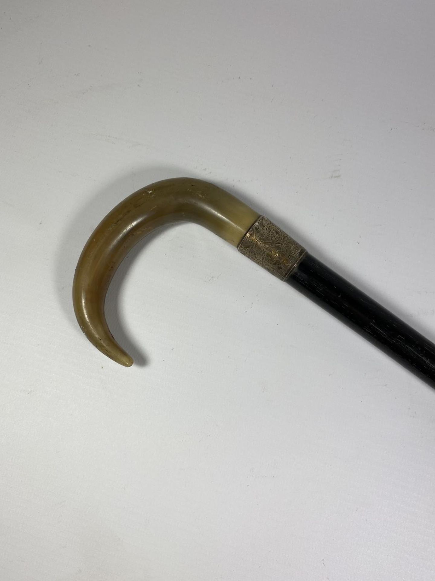 AN EDWARDIAN HORN STYLE HANDLED EBONISED WALKING STICK WITH BIRMINGHAM HALLMARKED SILVER FERRULE