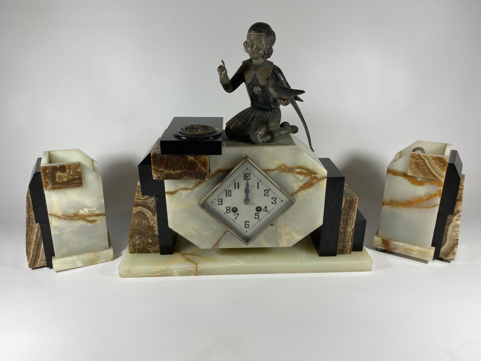 AN ART DECO MANTLE CLOCK WITH GIRL WITH BIRD FINIAL DESIGN AND SIDE GARNITURES