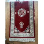 AN OBLONG RED PATTERNED FRINGED RUG