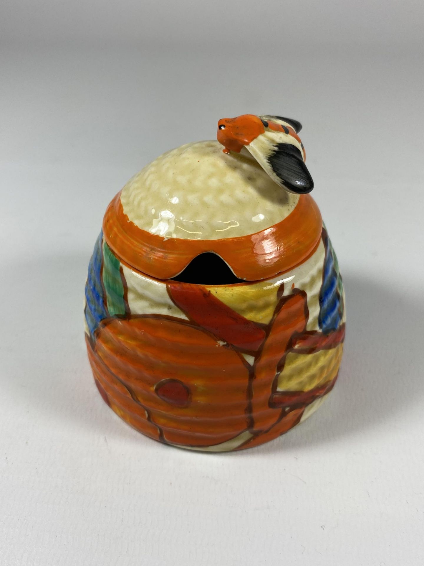 A CLARICE CLIFF CERAMIC HONEY POT IN THE 'FANTASQUE' PATTERN (CHIP TO RIM)