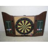A dartboard in wall hanging case along with two sets of darts