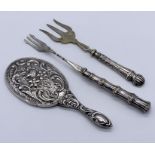 A Continental silver hand mirror along with a silver handled muffin fork and a pickle fork