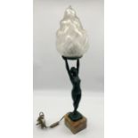 A green patinated Art Deco lamp in the form of a nude lady holding aloft a flame shaped glass