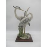 A ceramic figure of two herons on a wooden plinth, signed G. Armani.