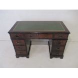 A reproduction kneehole desk with green leather top.