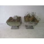 A pair of large weathered reconstituted stone garden planters on plinths, with floral motifs.