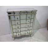 A mirrored chest of five drawers.