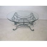 A low coffee table, with circular glass top on painted cast iron stand.