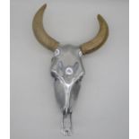 A polished aluminium wall sculpture in the form of a bull skull with wooden horns, height 54cm