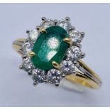 An 18ct gold emerald and diamond cluster ring, the central emerald measuring approx. 8 x 5 mm