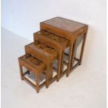 A nest of four Oriental carved oak tables, with glass tops.