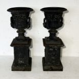 A pair of cast iron Grecian style urns on plinths - overall height 70cm