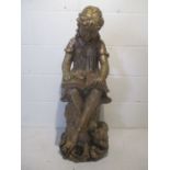 A painted resin garden figure of a young girl and her dog sat on a tree stump reading a book. Height