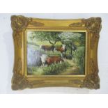 A gilt framed oil on board of cattle amongst trees