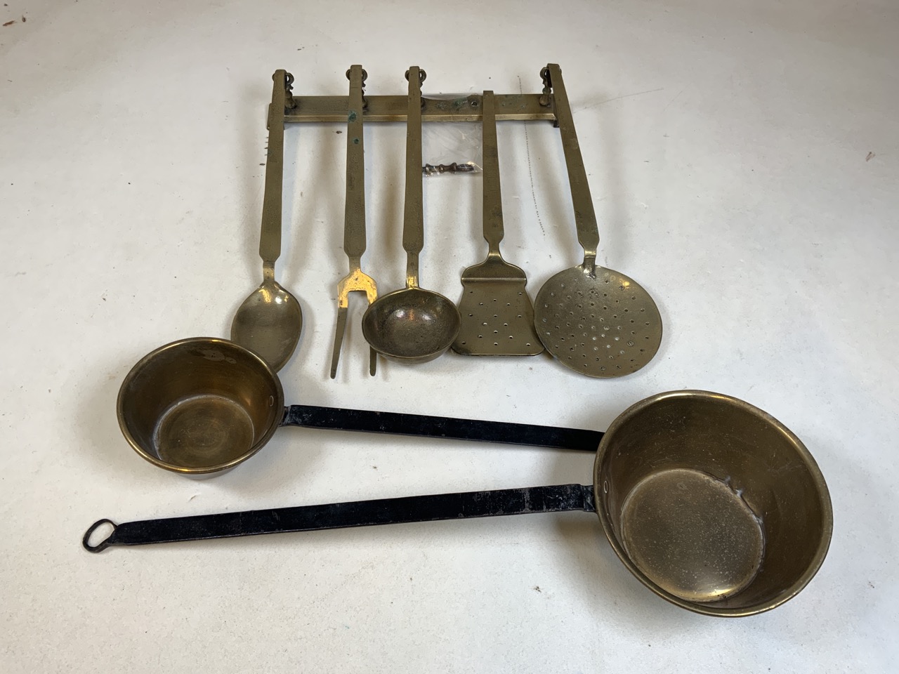 Vintage brass kitchenalia, a brass hanging rail with five utensils and two small brass pans with