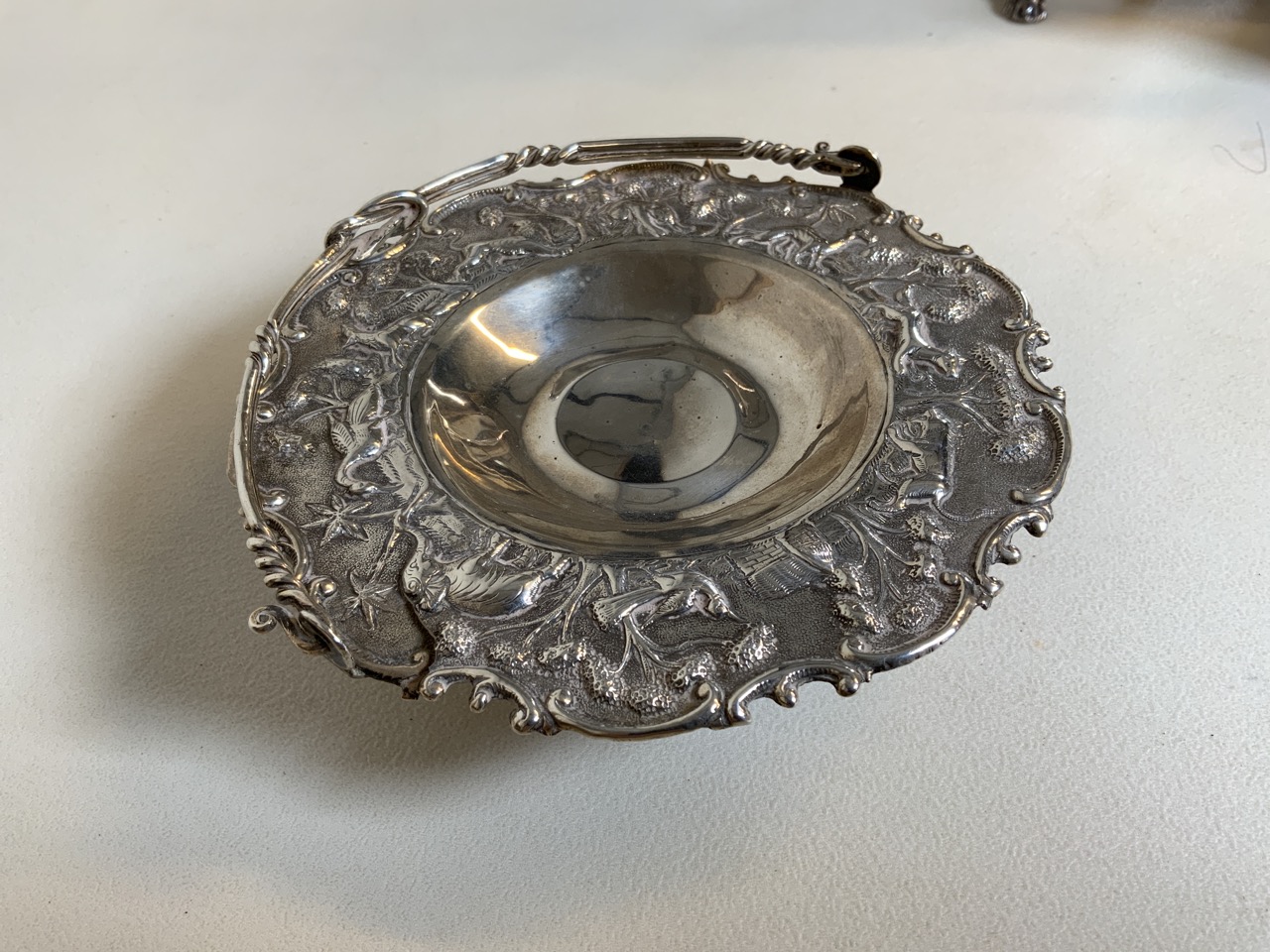 A Eastern white metal bon bon dish with carry handle. Decorated with wildlife.