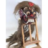 A Balinese ceremonial grotesque face mask in carved wood and painted in multi colours with horse