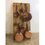 A set of 7 unlined copper saucepans on a presentation board. Largest pan 20cm W:43cm x H:89cm