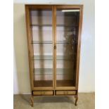 A mid century china cabinet with glazed doors to four glass shelves above two drawers with